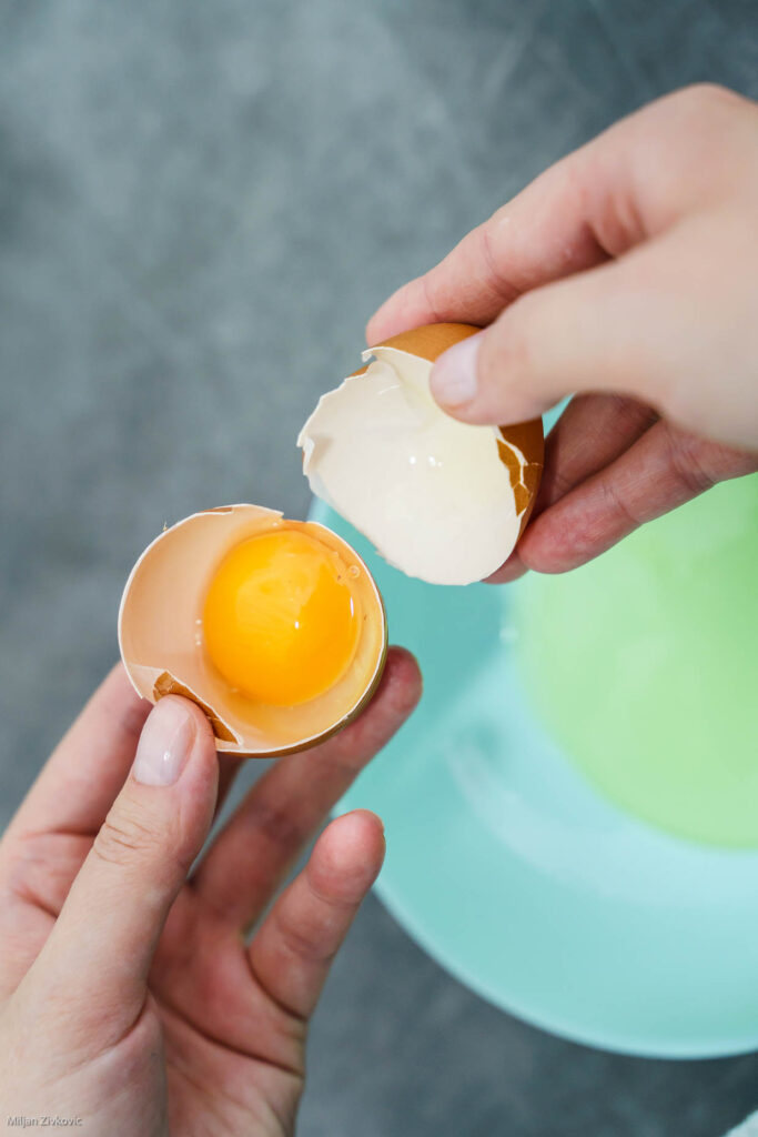 A pair of hands holding a cracked open egg over a bowl.