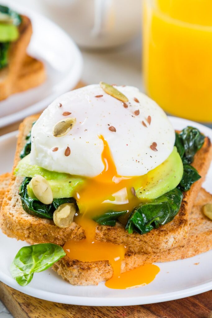 Close-up shot of a poached egg with yolk running out over toast that is topped with greens and avocado.