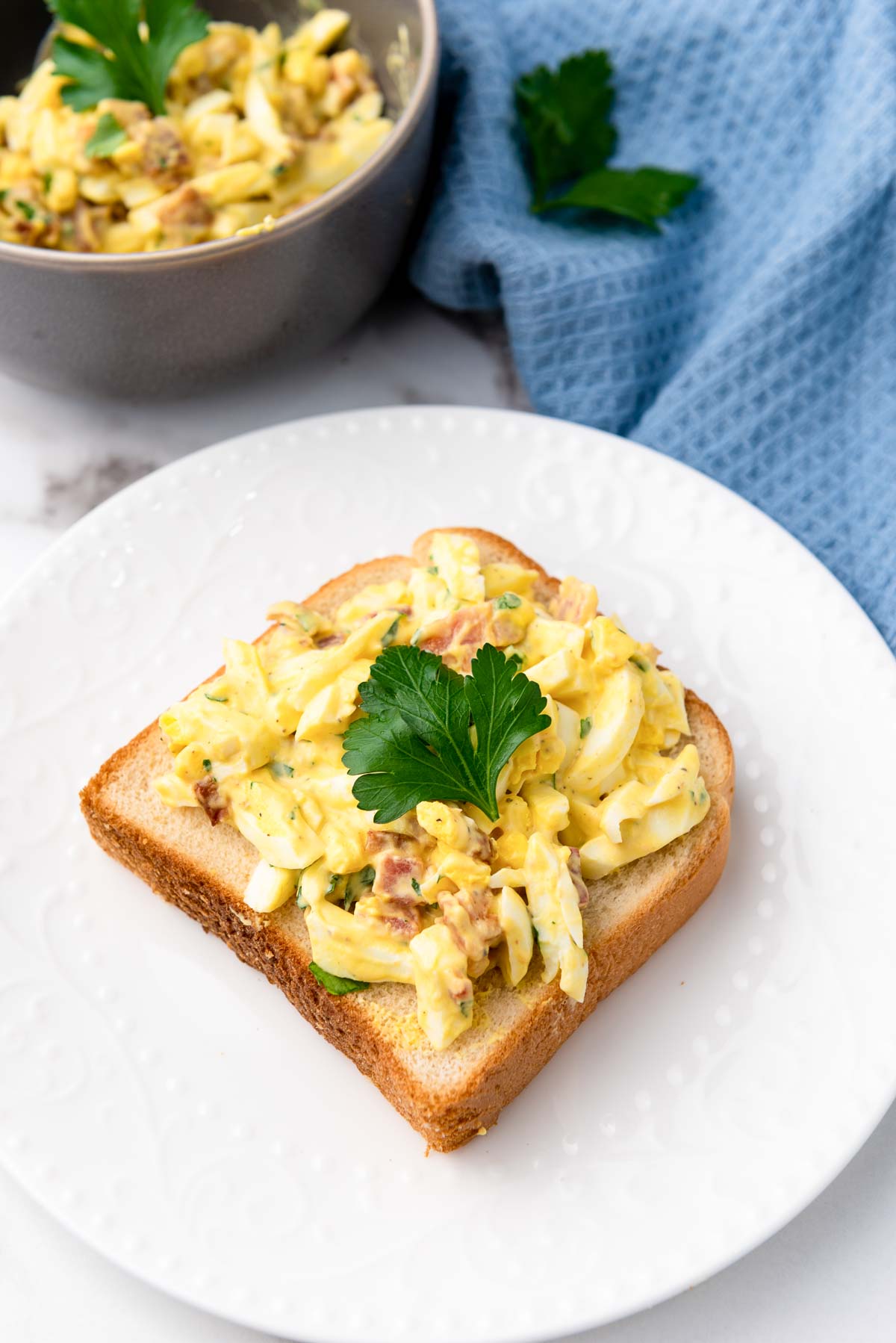 egg salad on a piece of white bread with parsley.