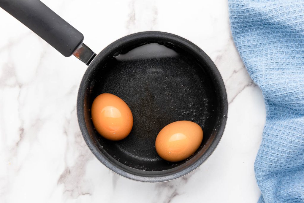 Two eggs in a frying pan with a blue towel, cooking over heat.