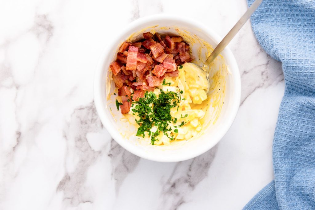 Scrambled eggs with bacon and parsley served in a white bowl.