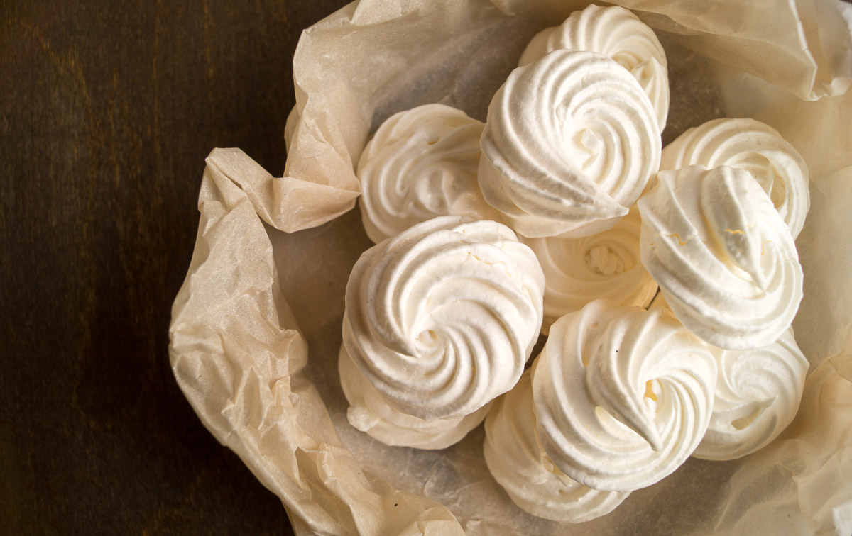 Learn how to make meringue by observing this fluffy treat served in a paper bag on a wooden table.