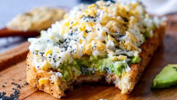 Avocado toast with black salt on a wooden cutting board.