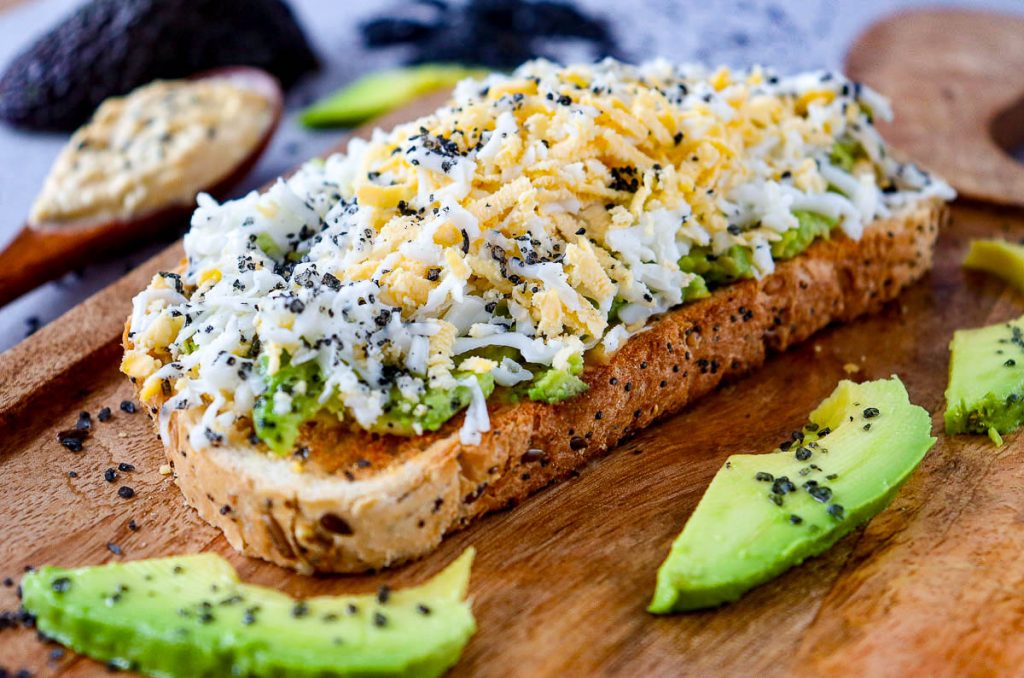 Avocado toast with grated egg on a wooden cutting board.