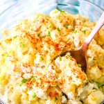 A bowl of creamy potato salad garnished with paprika and chives.