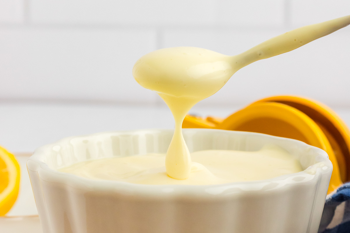 A spoon is pouring homemade mayonnaise into a bowl.