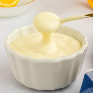 A person is pouring homemade mayonnaise into a bowl.