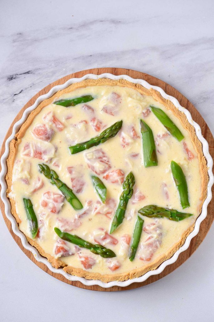 A quiche with asparagus and tomatoes on a wooden board.
