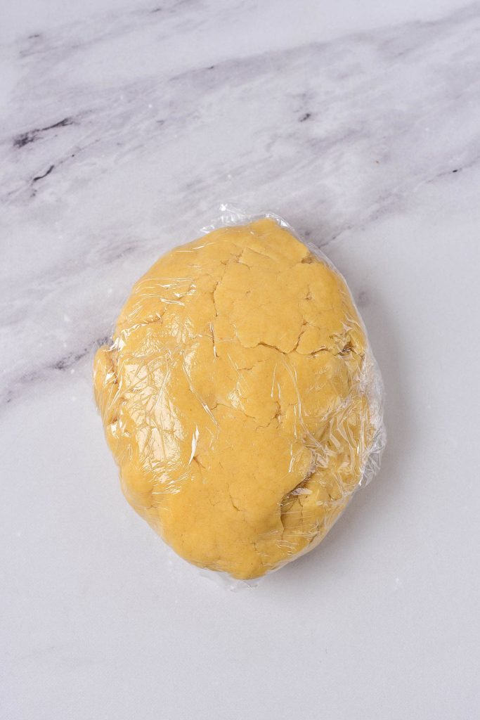 A dough ball wrapped in plastic on a marble table awaits to be turned into a quiche.