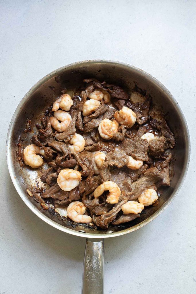A pan of stir-fried food with beef and shrimp.