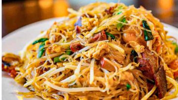 Close-up of a plate of Singapore noodles with shrimp, chicken, bean sprouts, peanuts, and green onions.