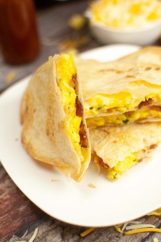 A breakfast quesadilla with eggs, bacon, and cheese, cut in half and served on a white plate.