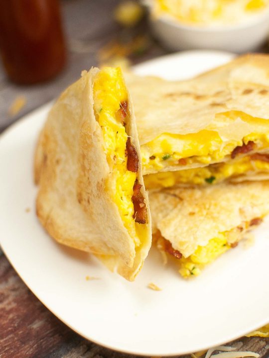 A breakfast quesadilla with eggs, bacon, and cheese, cut in half and served on a white plate.
