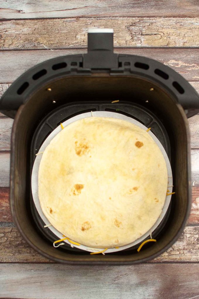 Top-down view of Breakfast Quesadillas inside an air fryer basket on a wooden surface.