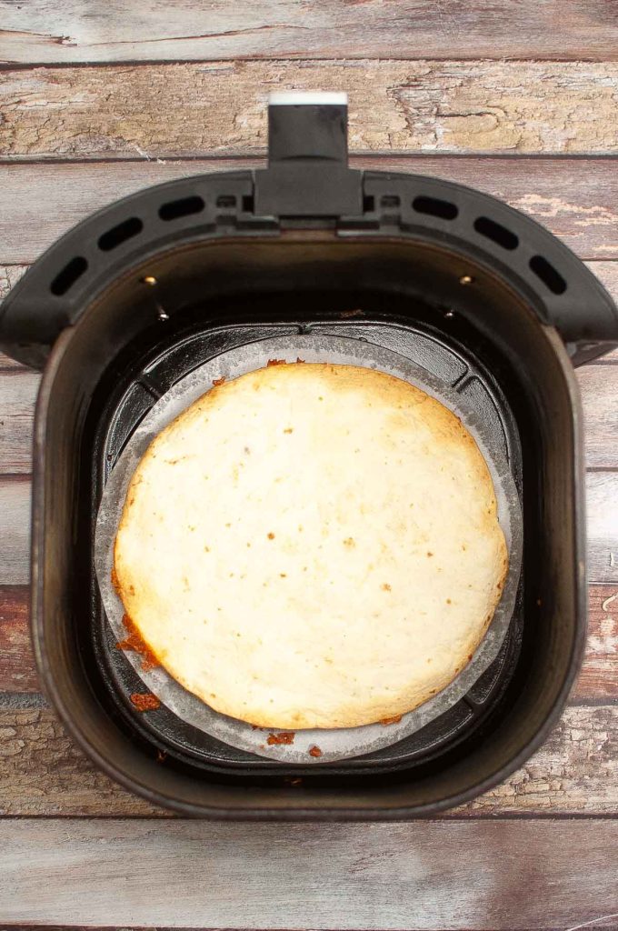 A large breakfast quesadilla inside an air fryer basket on a wooden surface.