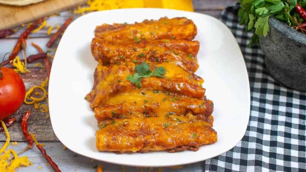 Plate of air-fried enchiladas with seasoned beef, parsley on a checkered tablecloth, with tomatoes and a yellow pepper in the background.