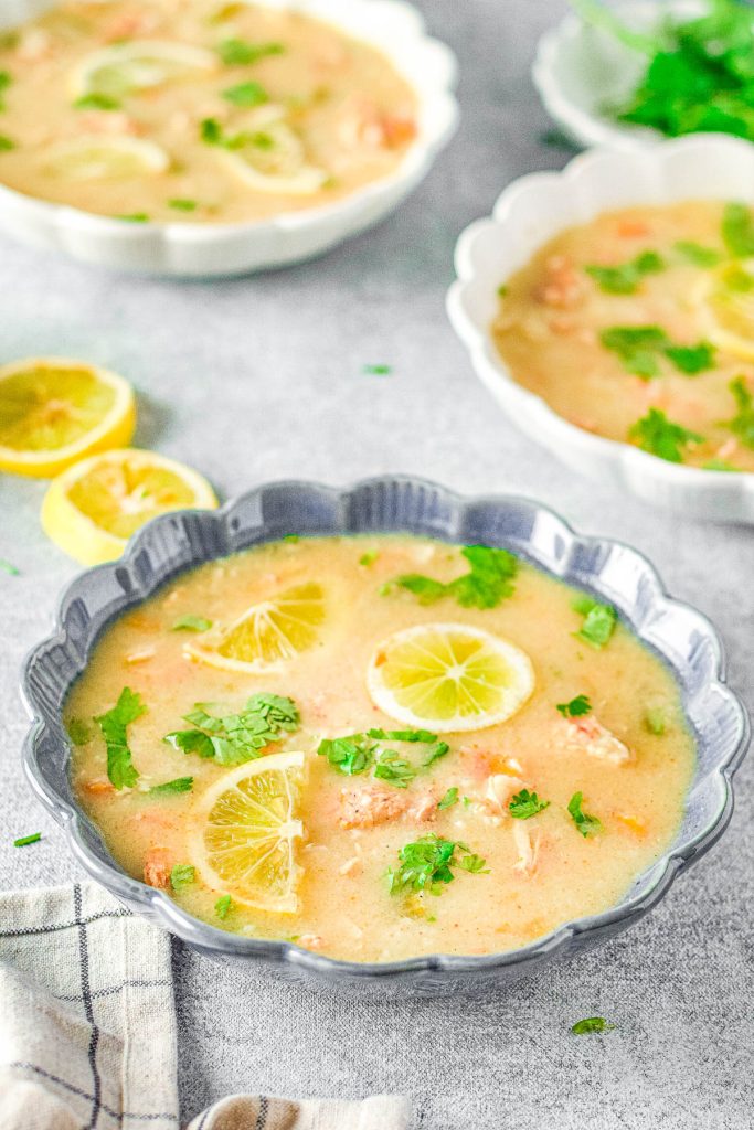 A vibrant bowl of Avgolemono Soup garnished with fresh parsley and lemon slices.