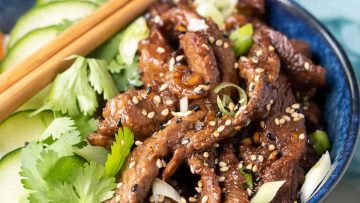 A bowl of beef bulgogi with cucumber slices, cilantro, sesame seeds, and chopsticks on the side.