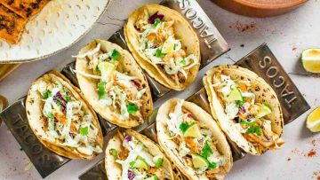 A selection of blackened fish tacos with various toppings served on metal stands with lime wedges and naan bread on the side.
