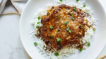 A plate of white rice topped chicken egg foo young, garnished with chopped green onions.