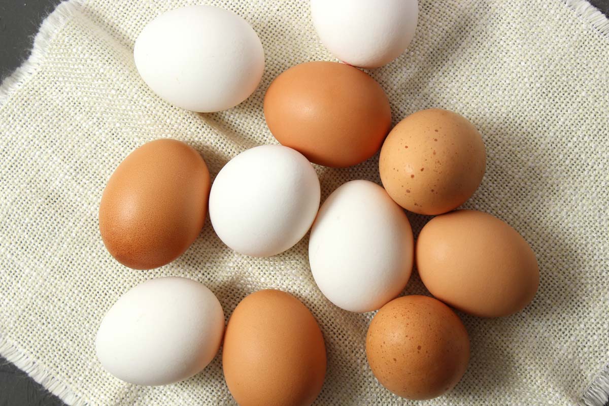 A collection of farm-fresh brown and white eggs on a beige cloth, shot from above.