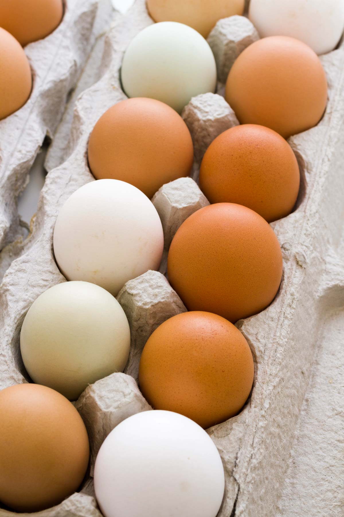 A carton of eggs, various colored eggs, including shades of brown, white, and pale green, arranged in a pattern.