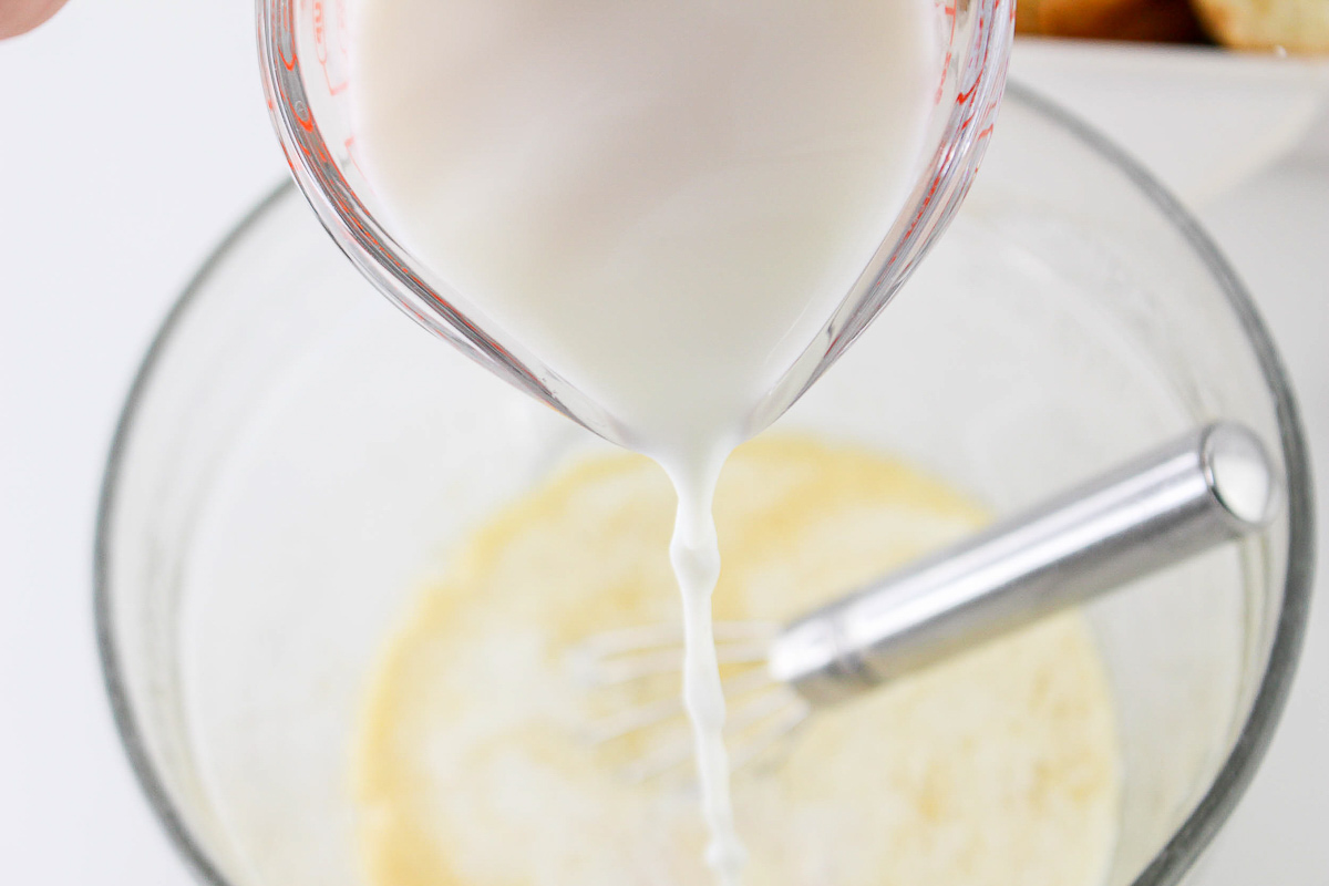 Pouring milk into a bowl containing a whisk and a mixture for Breakfast Recipes.