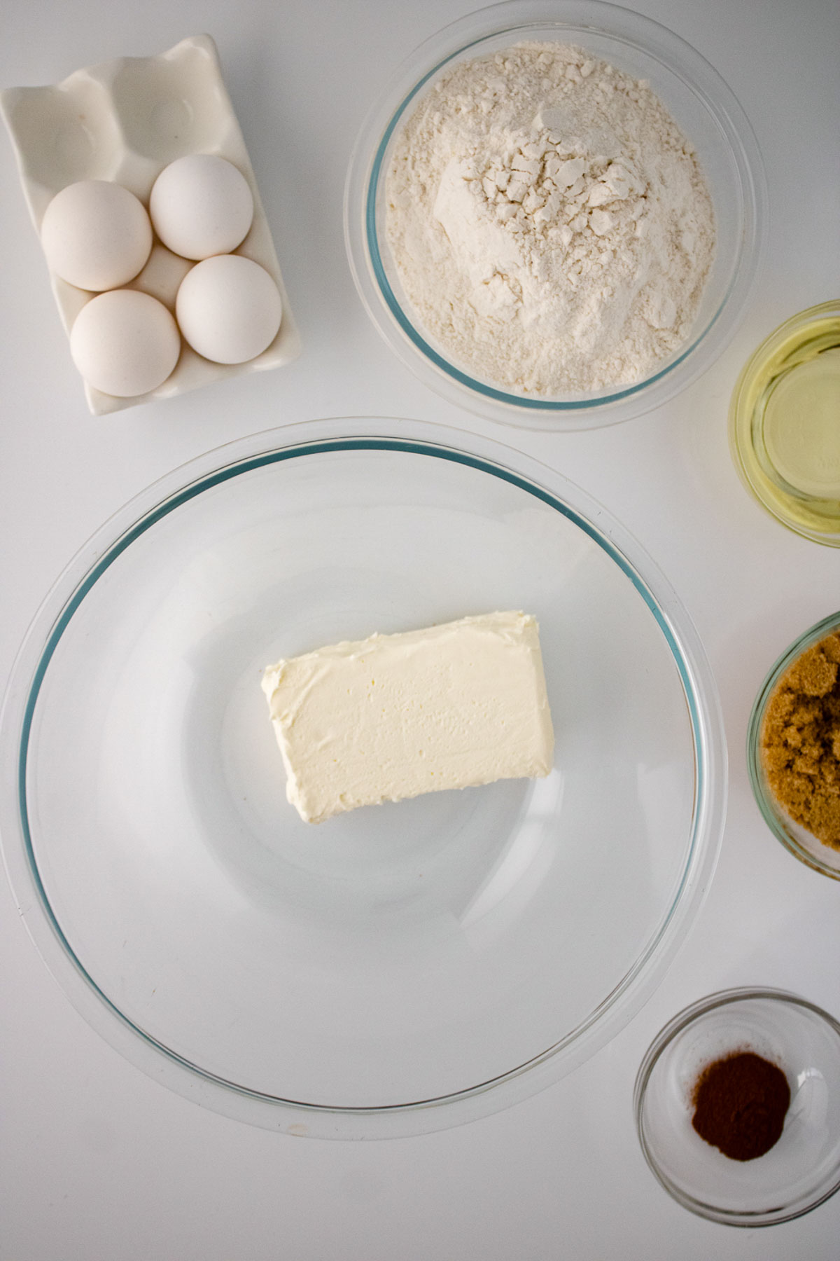 Top-down view of dessert baking ingredients on a white surface, including eggs, flour, butter, sugar, and cinnamon in separate bowls.