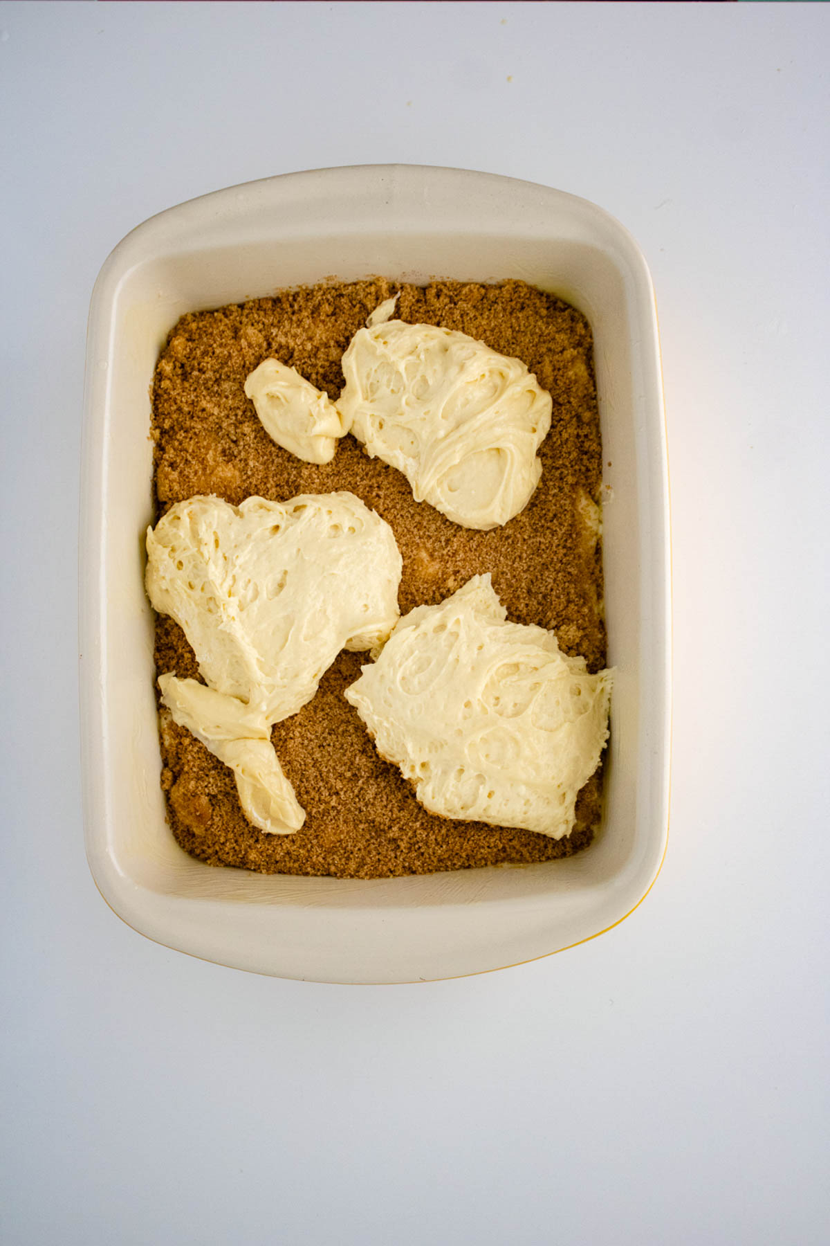 A rectangular baking dish with a layer of brown crumble topped with four dollops of white cream shaped like leaves, perfect for any dessert recipe.