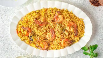 A plate of shrimp biryani with rice, shrimp, and spices, served on a white plate, displayed on a light-colored textured surface.