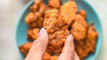 A person holding a fried mochiko chicken over a plate of more mochiko chicken.