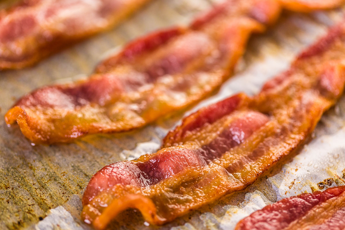 Strips of crispy oven bacon cooking on a pan.