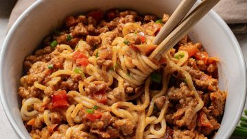A bowl of peanut sauce beef and ramen noodles, garnished with herbs and chopped tomatoes.