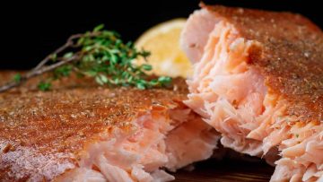 Close-up of a smoked salmon filet garnished with thyme and a slice of lemon.
