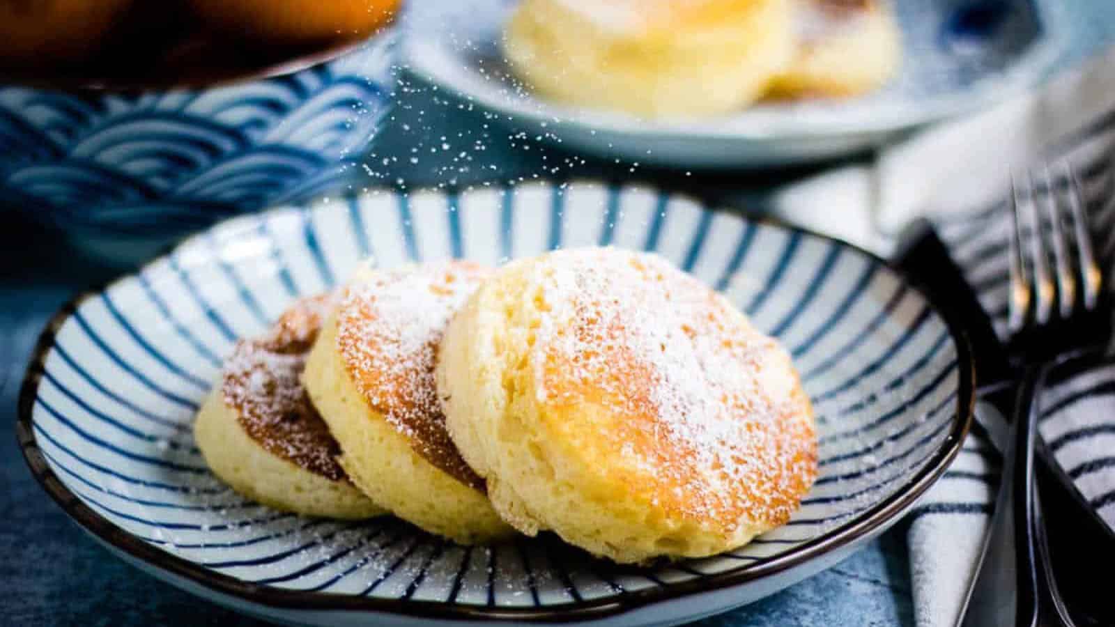 Three souffle pancakes with powdered sugar on a blue and white striped plate.