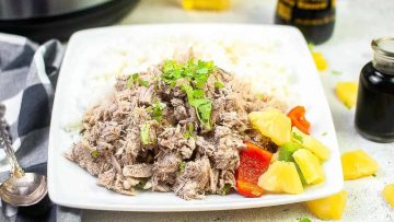 A plate of shredded meat garnished with fresh herbs, served with rice and a side of chopped bell peppers and pineapple.
