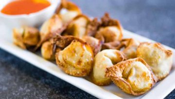 A plate of golden fried wontons served with a side of red dipping sauce.