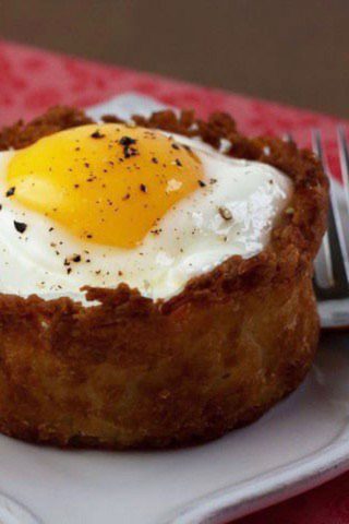 A sunny-side-up egg resting on a crunchy potato crust, seasoned with pepper, on a white plate.