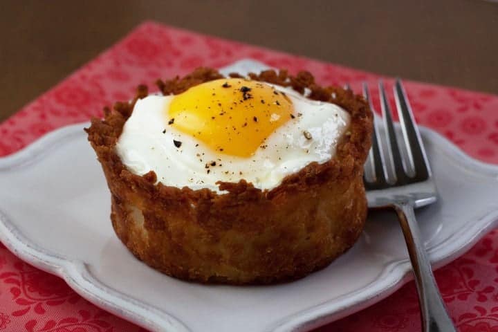 Baked egg in a crust made of shredded potatoes on a plate.