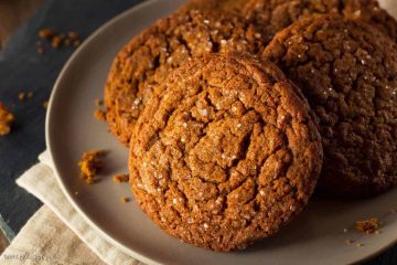 A plate of homemade chewy molasses cookies with sugar crystals on top, set on a dark surface.