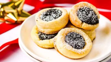 A plate of poppy seed-filled cookies dusted with powdered sugar, displayed on a red and white festive background.