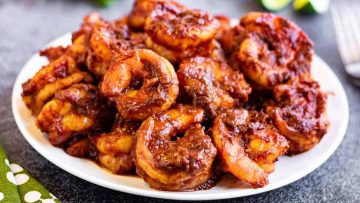 A plate of spicy, marinated shrimp cooked in a reddish sauce is arranged on a white dish—a Sunday Dinner must-have.