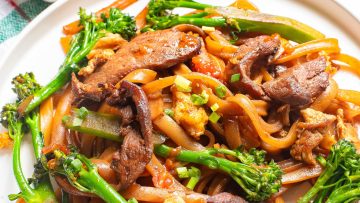 A plate of stir-fried noodles with beef strips, broccoli, and scallions on a white dish.