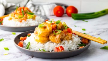 Plate of rice topped with shrimp and diced tomatoes, garnished with green onions. Chopsticks are placed on the side.