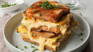 A stack of delicious breakfast sandwiches piled high on a plate, each egg sandwich grilled to perfection and garnished with chopped green onions and parsley.