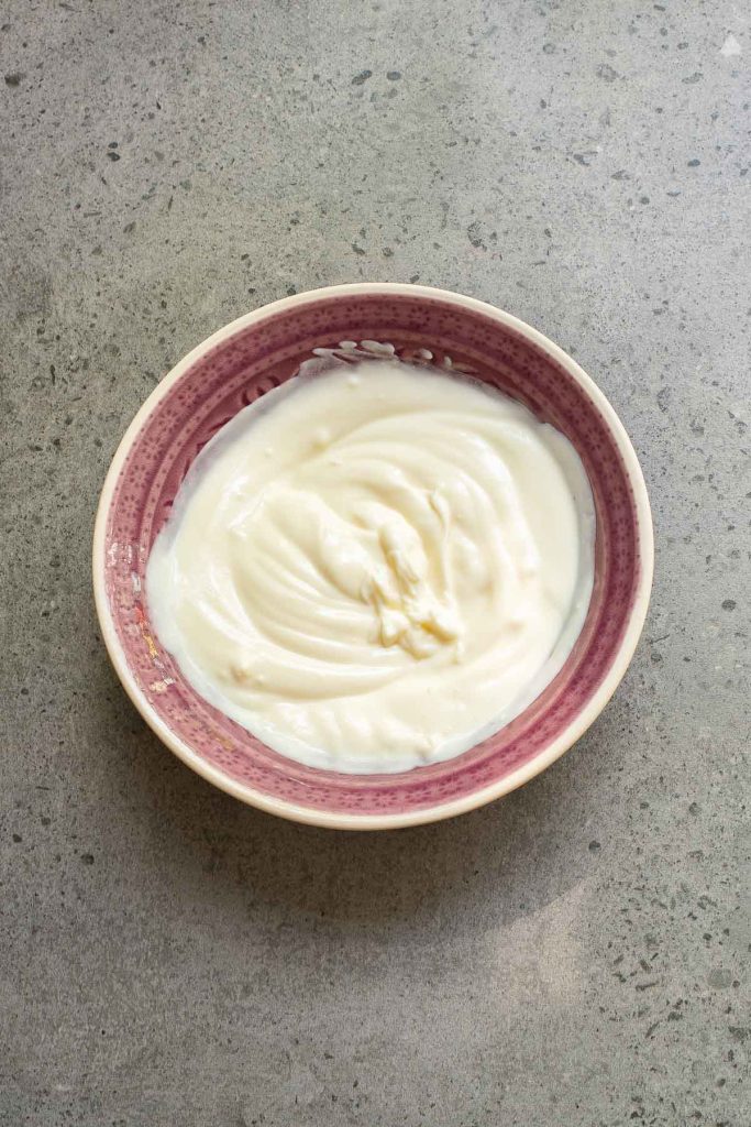 A bowl filled with smooth, creamy garlic yogurt sits on a gray speckled countertop.
