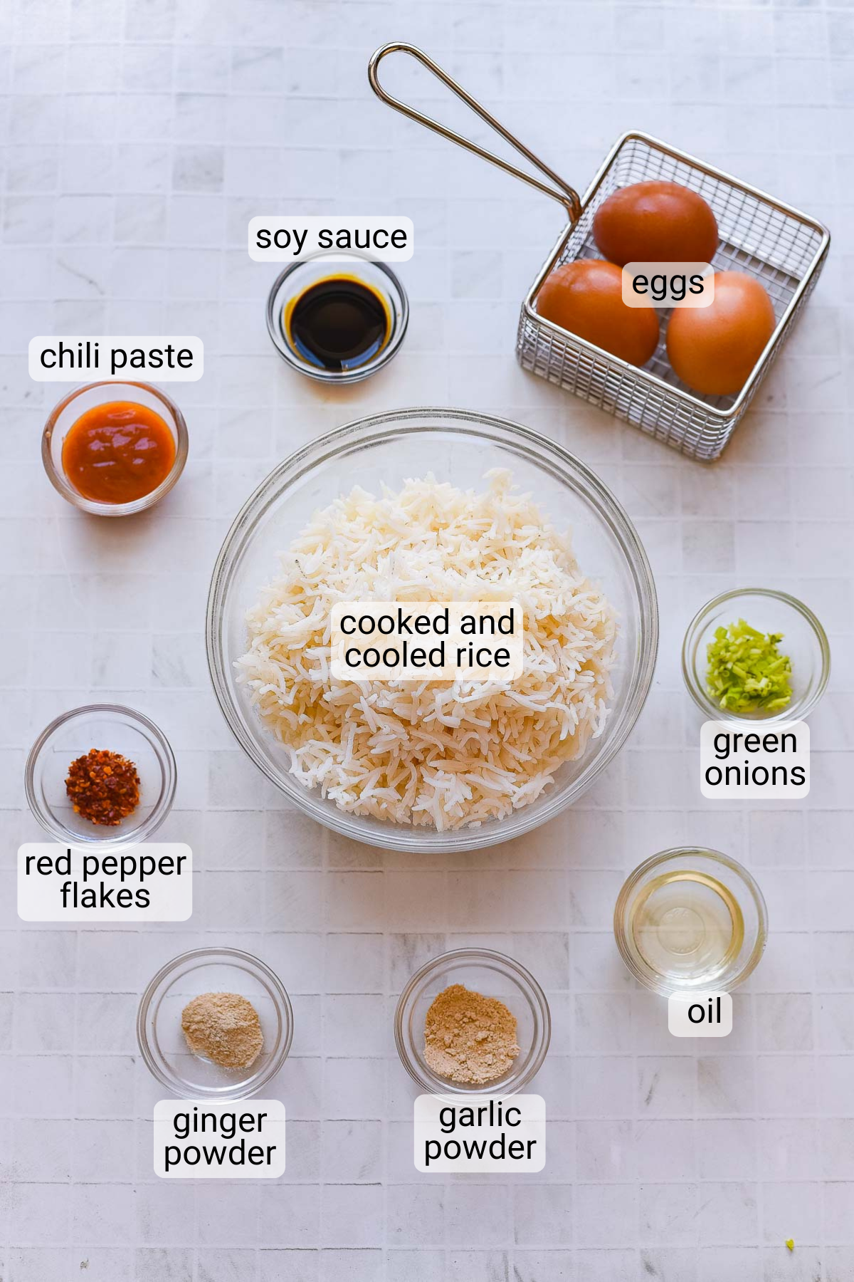 Top-down view of ingredients for Spicy Egg Fried Rice, featuring cooked rice, eggs, soy sauce, chili paste, green onions, oil, red pepper flakes, ginger powder, and garlic powder.