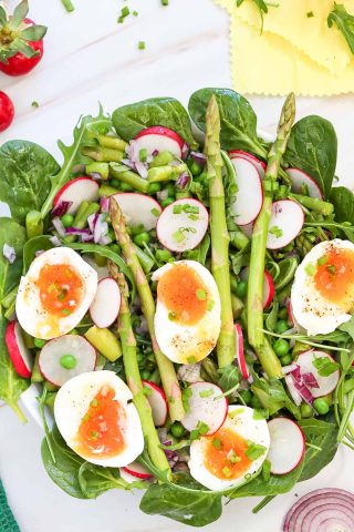 A vibrant pea salad with spinach, sliced radishes, asparagus spears, chopped red onion, green peas, and halved soft-boiled eggs on top.