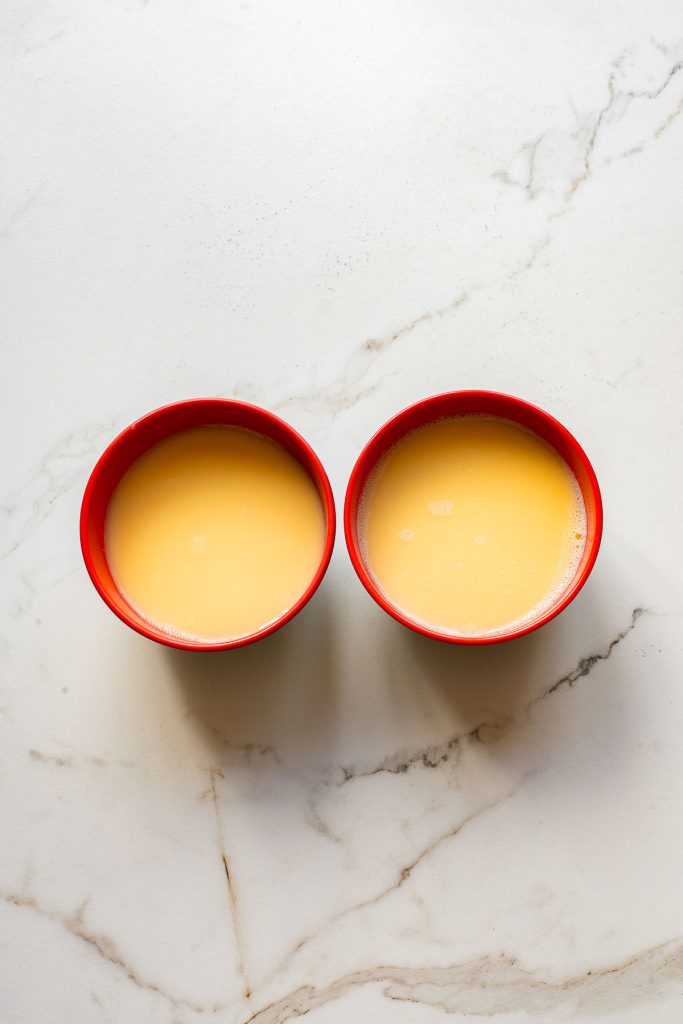 Two red bowls filled with delicate Chinese Steamed Egg sit side by side on a white marble surface, showcasing the classic silky-steamed egg custard.