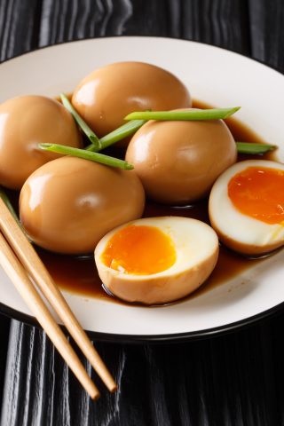 A plate of soy-marinated soft-boiled eggs, some halved showing runny yolks, garnished with green onions and served with wooden chopsticks.